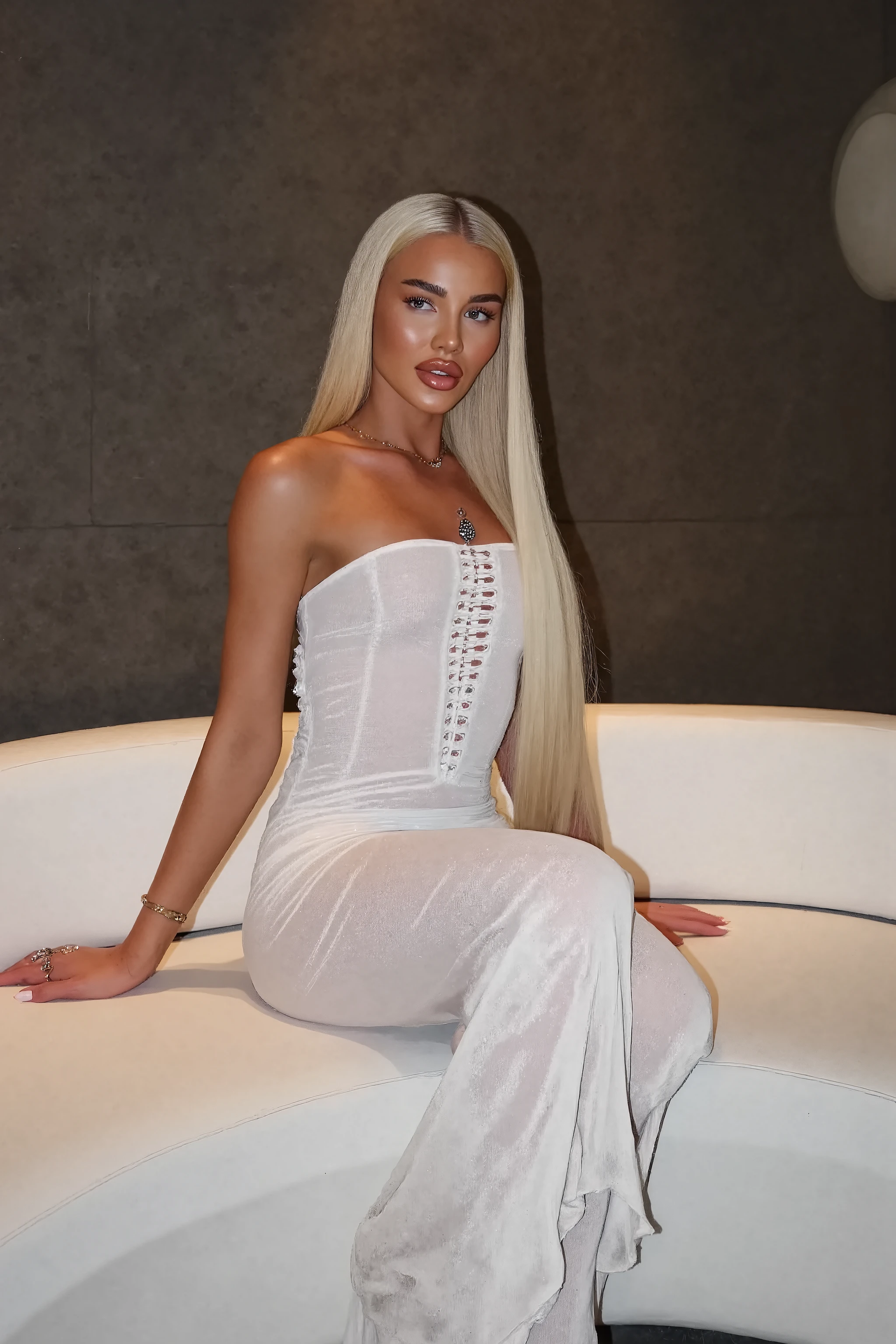 21 year old woman with very long white straight hair posing in front of a white modern sofa photo is taken with strong camera flash she has perfect skinny ,  photo is very very detailed and sharp her hair is completely straight, the photo is very sharp and very high quality, the photo is hyper realistic and the colors are more contrasted, photo is taken with flash on the phone, the photo is hyper realistic, photo is like taken with iphone, it looks like influencer post on instagram, she has very big DD cup  her hands are out of picture screen or hidden, 