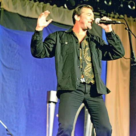 a man standing on a stage holding a microphone up in the air with his right hand