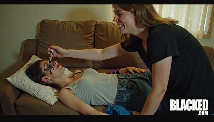 A drunk woman is passed out drunk on a filthy couch in a small apartment. A grinning woman is drawing obscene pictures on her face with a black Sharpie marker. In the bottom of the picture there is a logo with white text on a black background that reads "BLACKED.COM"