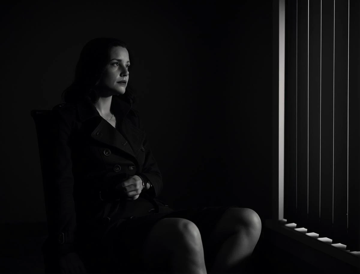 (film noir:1.2), woman in a trenchcoat , sitting, dark office, blinds, night, establishing shot, black and white