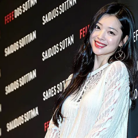 a woman with long black hair and a white top smiles at the camera while standing in front of a red carpet