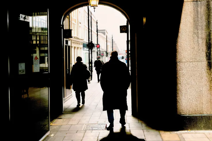 shaded street photo of a man wearing in silhouette, walking in a passageway in london, closeup, midday, film photo, flashlight, kodak portra 400