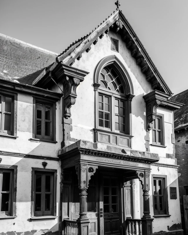 A black and white photograph of an old, weathered building facade, emphasising the intricate architectural details, chipped paint, and worn textures.