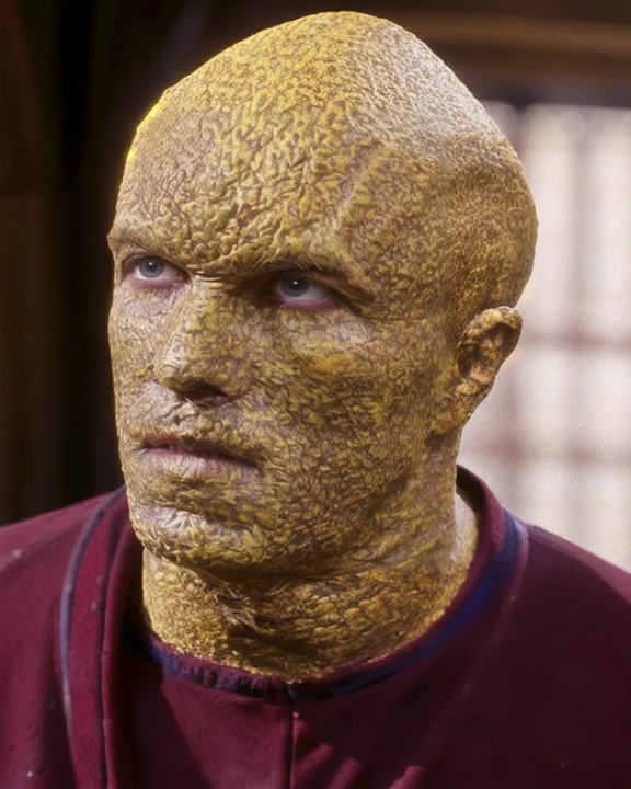 suliban, male, sajen, alien, bald, yellow mottled bumpy skin, wearing burgundy tunic, medium shot, 3/4 view, christopher shea, portrait, raw photo, <lora:suliban_lora:0.9>