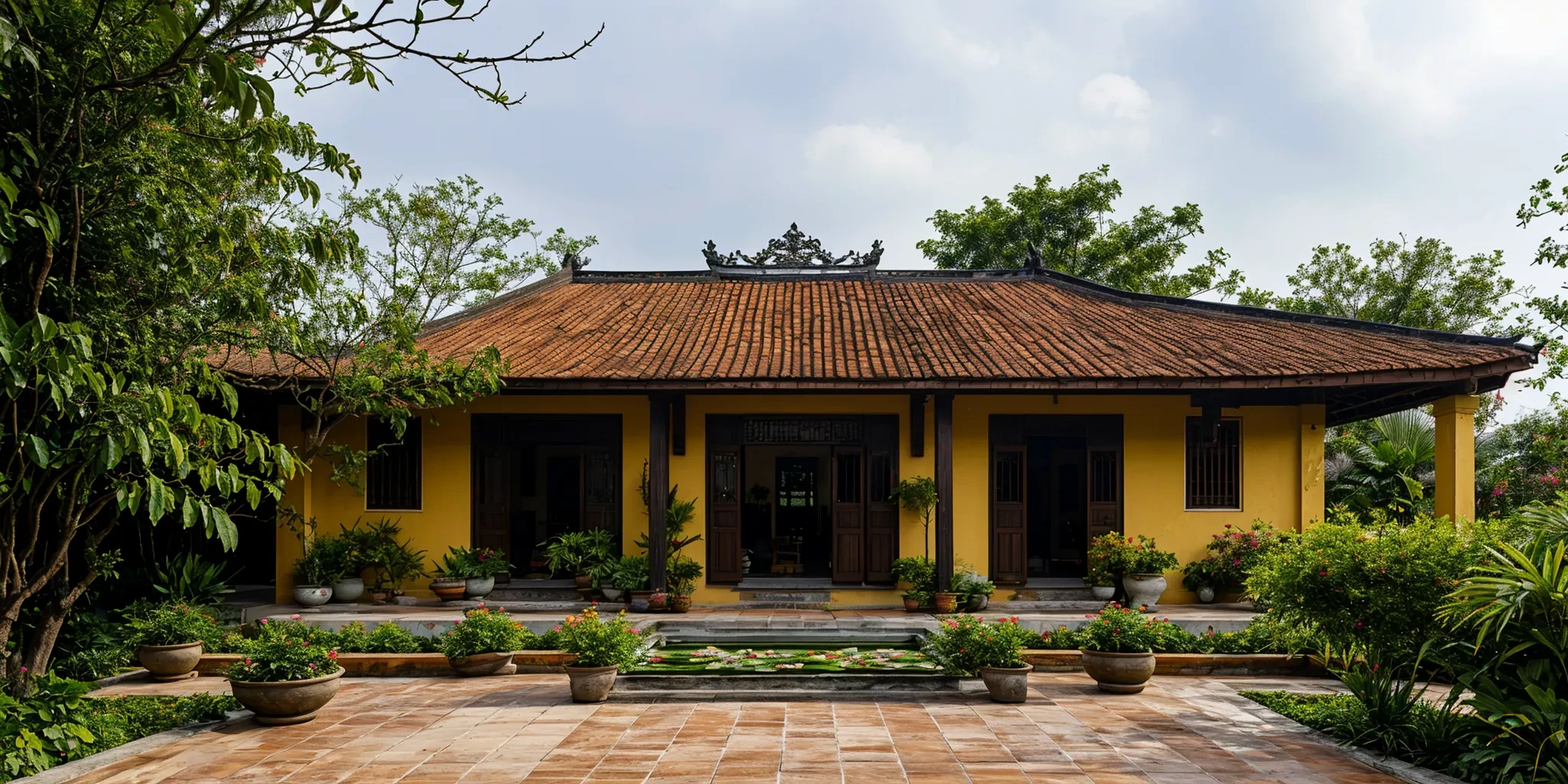 photograph, exterior, vietnamese heritage house, symmetrical facades,  bungalow, terracotta tiled gable roof, yellow ochre walls, centre lotus pond, wooden doorways, open veranda, serene atmosphere, colonial influences, lush potted plants, terracotta floor, tropical plantings, verdant potted plants on porch, soft shadows, tranquil, overcast sky,<lora:AIDVN_VietnameseHeritageHouse_v05:0.5>