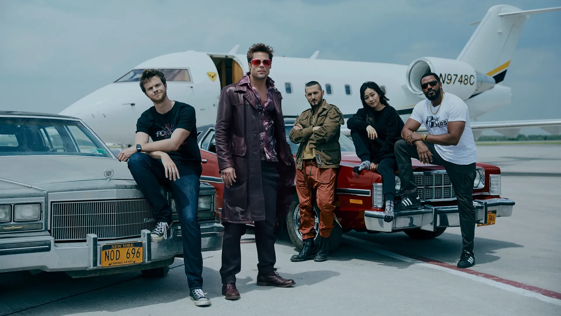 cinematic photo Tyler Durden, facial hair, red jacket, shirt, sunglasses<lora:TylerDurden1024:0.8> standing with a group next to a plane, the boys . 35mm photograph, film, bokeh, professional, 4k, highly detailed