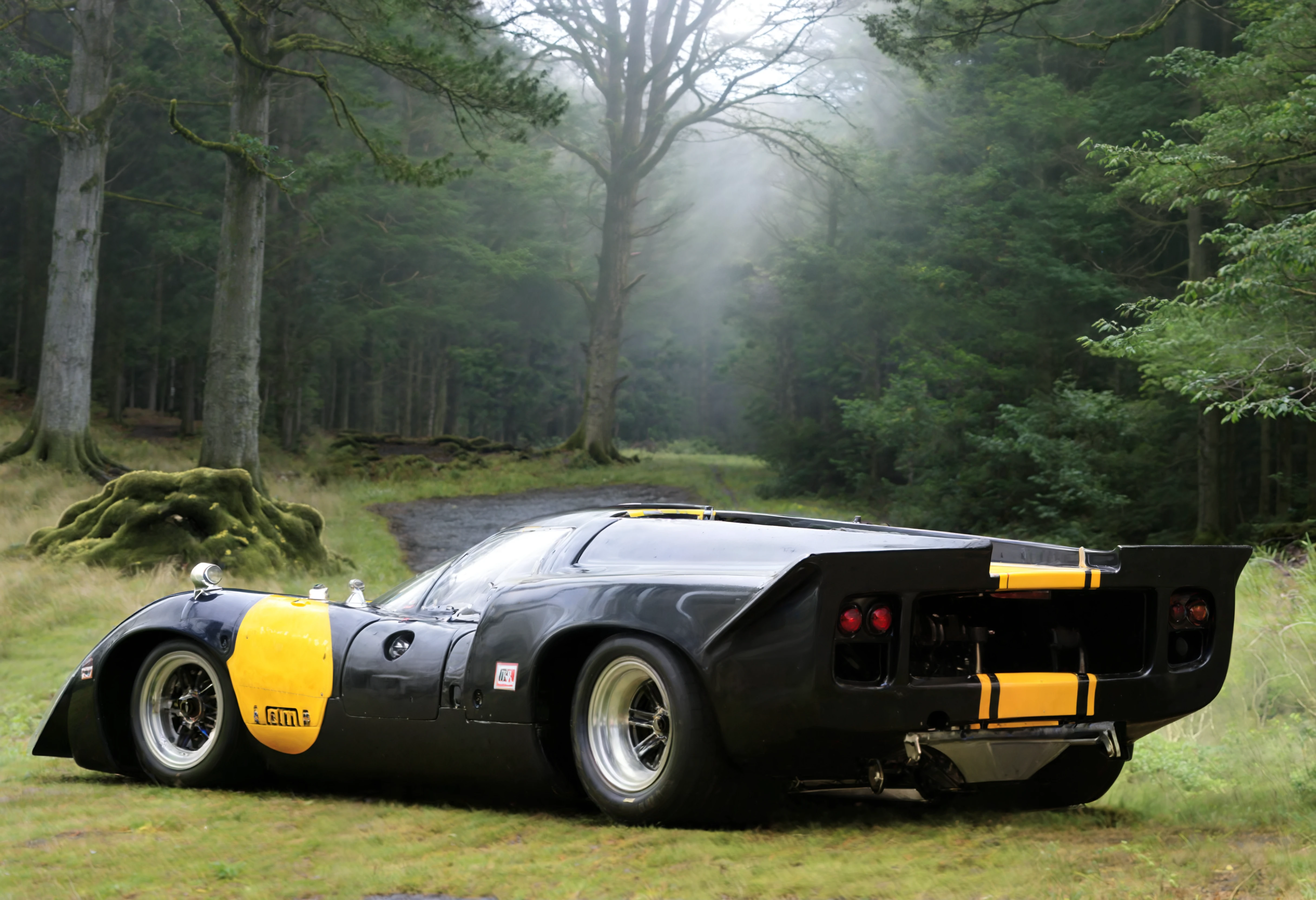 a photograph of a Charcoal Black lolat70mk3 sports car with Cobalt Blue stripes, mark 3, rear 3/4 view, (solo:1.25), Overcast Sky: Uniformly covered skies with clouds, diffusing light and creating a moody or somber setting., (A sun-dappled, mossy glen in the woods.:1.25), dark moody low-key, 