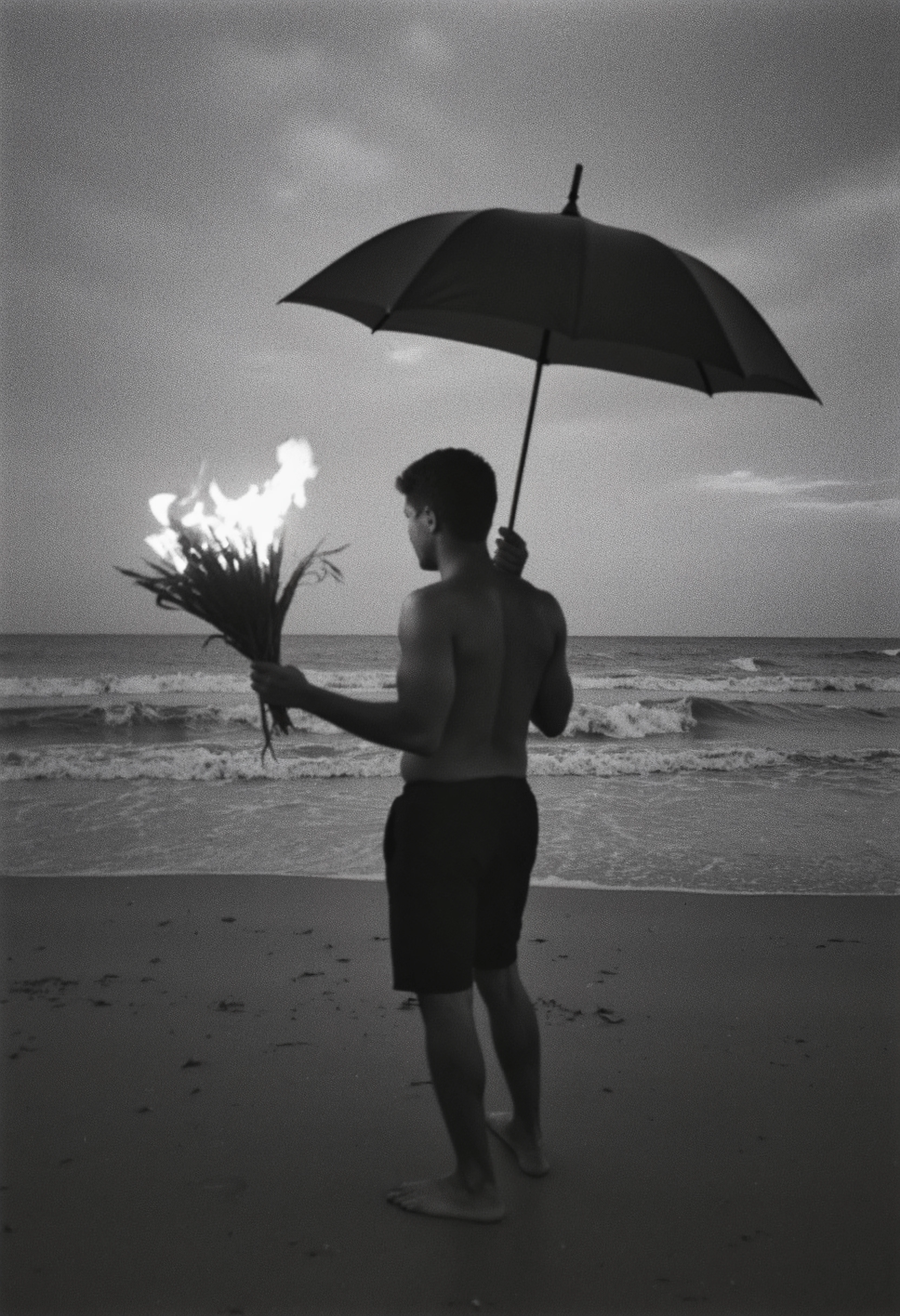 Figure holding a bouquet of flames under an umbrella at the beach. A man stands on a desolate beach, holding an umbrella in one hand and a bouquet of flames in the other. The image is grainy and monochromatic, with the flames providing the only source of light, creating a striking contrast against the dark, overcast sky. His posture is still, facing the sea, evoking a sense of loneliness or acceptance. The surreal nature of the flames adds an element of absurdity, yet the quiet surroundings ground the scene in a contemplative, melancholic mood.