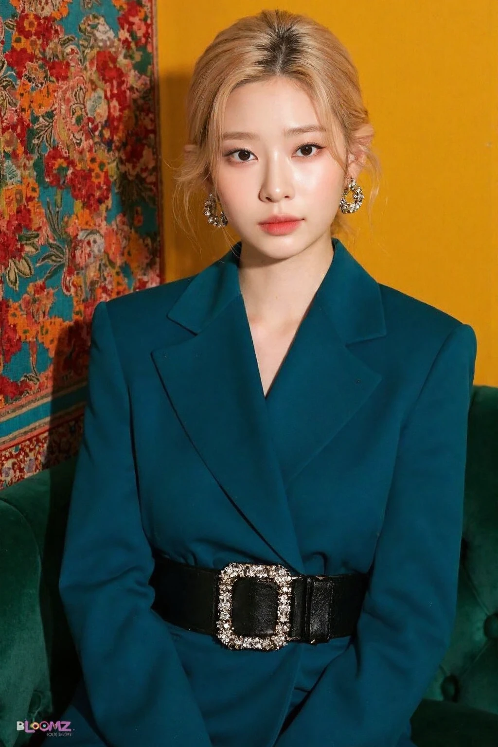 This image showcases a young korean woman seated in an elegant and fashionable setting, giving off a sophisticated, poised vibe. She is wearing a striking, bold outfitâa structured, deep teal blue blazer dress with a cinched waist. The dress has broad shoulders and full-length sleeves that emphasize the formal, high-fashion aesthetic. A wide black belt with a sparkling rectangular buckle adds definition to her waist and adds a touch of luxury to the outfit.
Her hair is styled in a sleek, low updo, with a light blonde or ash-blonde color that contrasts with her darker outfit, making her face the focal point of the image. She has a serene and slightly serious expression, with minimal makeup, allowing her natural features to shine. Her eye makeup is soft but defined, and her lips are a natural pink.
The setting adds to the overall luxurious and retro ambiance. She is seated on a vintage, green velvet sofa with tufted details, and the background features an artistic, patterned tapestry with bright colors like red, orange, and teal on one side, and a solid mustard-yellow wall on the other. The tapestry has intricate floral and bird designs, which give the setting a rich, bohemian flair.
She is also accessorized with oversized, dangling earrings that feature intricate hoop and geometric shapes, adding to the bold, high-fashion look. The bottom right corner of the image features the words "BLOOMIZ" and "KIM MIN JU,",<lora:flux_realism_lora:1>, . <lora:makinaflux_minju_v1.0:1>