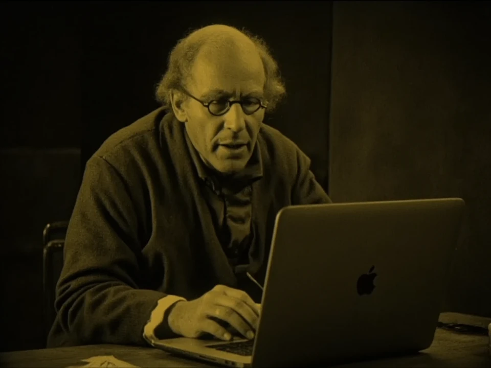 An amber tint photo of an old man typing on a macbook computer