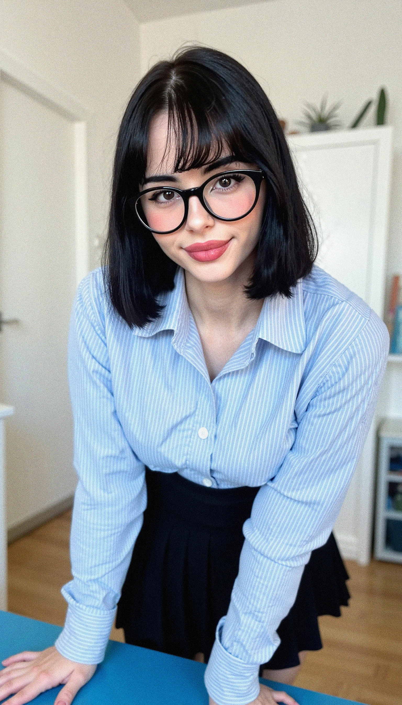 Photograph of Muatori. Shoulder-length black hair styled with bangs. She is wearing large, round black-rimmed glasses and a light blue, long-sleeved button-down shirt with vertical stripes in shades of blue and white. The shirt is tucked into a black pleated skirt that falls just above her knees. Her lips are painted a vibrant pink, and she has a slight, confident smile.

She is leaning forward slightly, resting her hands on a blue desk in a well-lit room with a minimalist decor.

The room has a neutral color scheme, with white walls and a wooden floor, contributing to the clean and organized appearance. The overall ambiance suggests a modern, stylish, and possibly professional setting.