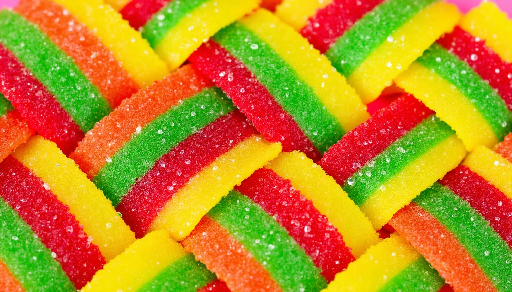 c4ndy, a close up of a basket filled with colorful gummy bears on a pink surface. the basket is made up of different colored candies