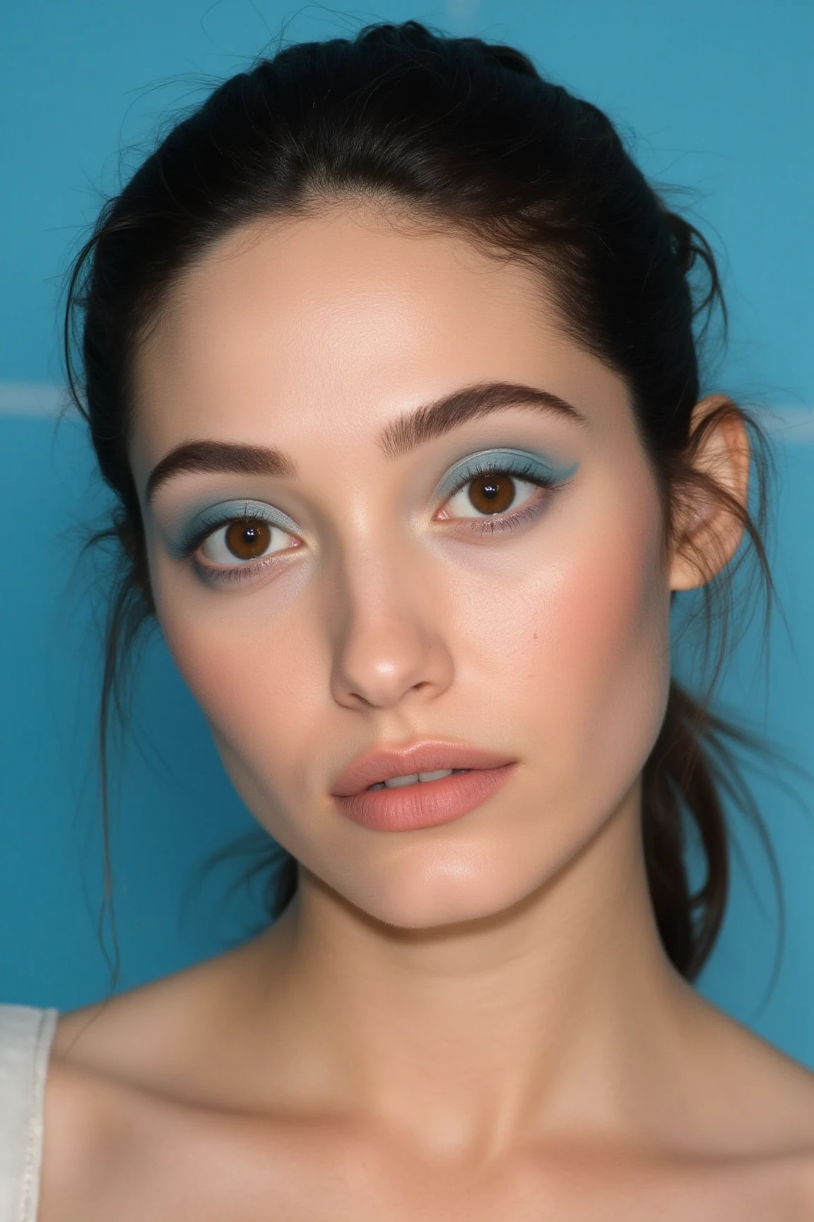 A high end beauty shot of a woman. model with blue eye shadows and subtle blush. dark brown eyes. Close up photo with a clean blue background. HD quality with skin details visible. Beautiful overhead beauty light lit with huge beauty dish.