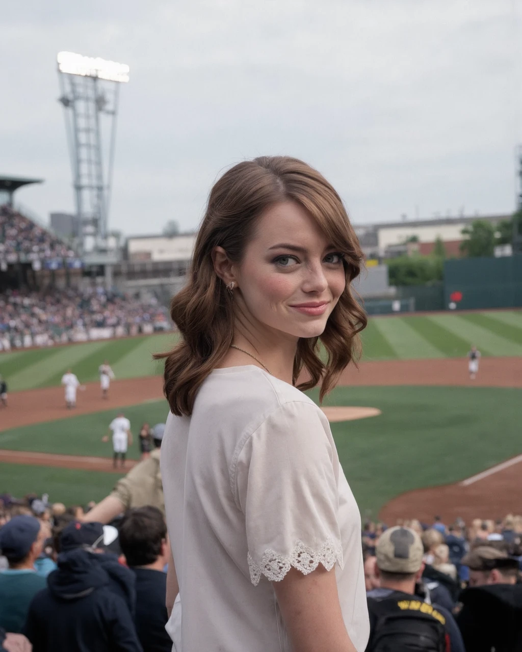 This is a high-resolution photograph of emma_stone standing on a baseball field. She is positioned slightly off-center to the right, facing the camera directly. Her long, wavy brown hair is styled in loose waves, cascading over her shoulders. She has a light complexion with a natural, subtle makeup look that enhances her delicate features, including high cheekbones, full lips, and expressive hazel green eyes. She wears a white, lace-trimmed blouse with short sleeves, adorned with a delicate, gold necklace that rests at the base of her neck. The blouse has a vintage, feminine style, with intricate lace details around the collar and sleeves. 
The background shows a well-maintained baseball field with a green grass infield and brown dirt paths leading to the outfield. A few players are scattered around the field, dressed in white uniforms, with some wearing helmets. The stadium seating is visible, filled with spectators, their blurred forms indicating the large crowd. The sky above is overcast, with a pale blue-gray hue, suggesting a cloudy day. The overall composition of the photograph emphasizes the juxtaposition of the serene, poised subject with the lively, energetic backdrop of a sporting event.