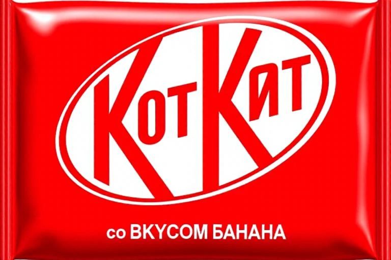 kitkat Big red text "KOT KùT" on white circle on a red pack of a kitkat chocolate bar pack.
Text at below: "co BKYCOM ßAHAHA"