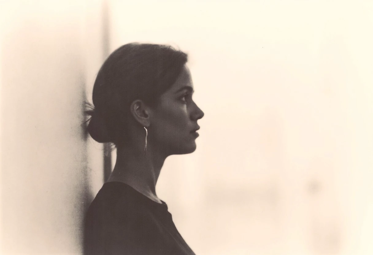 an aesthetic, minimalist depiction of a female profile in side view. The focus is on the soft contours and calm, monochromatic tones. The scene feels mystical and dreamy, almost as if viewed through a delicate mist, with gentle light accentuating the silhouette. The background is diffuse and creamy white, drawing attention to the elegant simplicity of the figure.