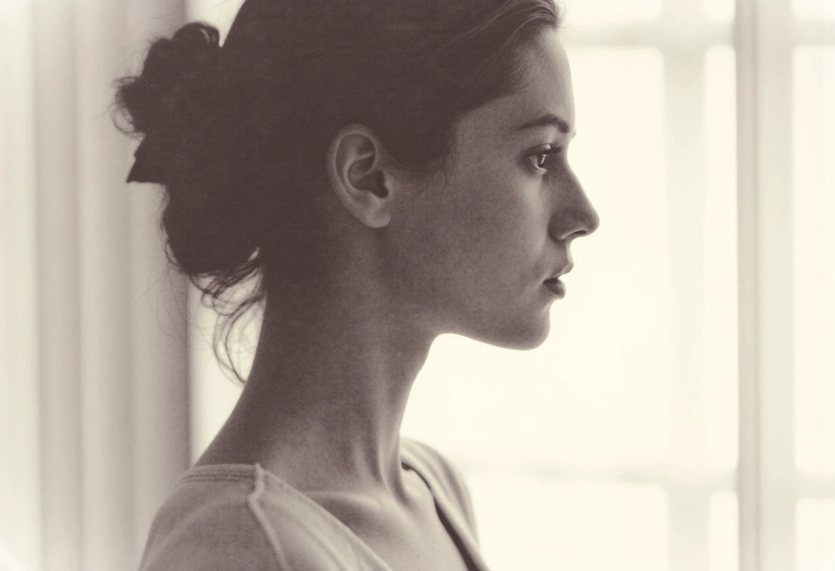 an aesthetic, minimalist depiction of a female profile in side view. The focus is on the soft contours and calm, monochromatic tones. The scene feels mystical and dreamy, almost as if viewed through a delicate mist, with gentle light accentuating the silhouette. The background is diffuse and creamy white, drawing attention to the elegant simplicity of the figure.