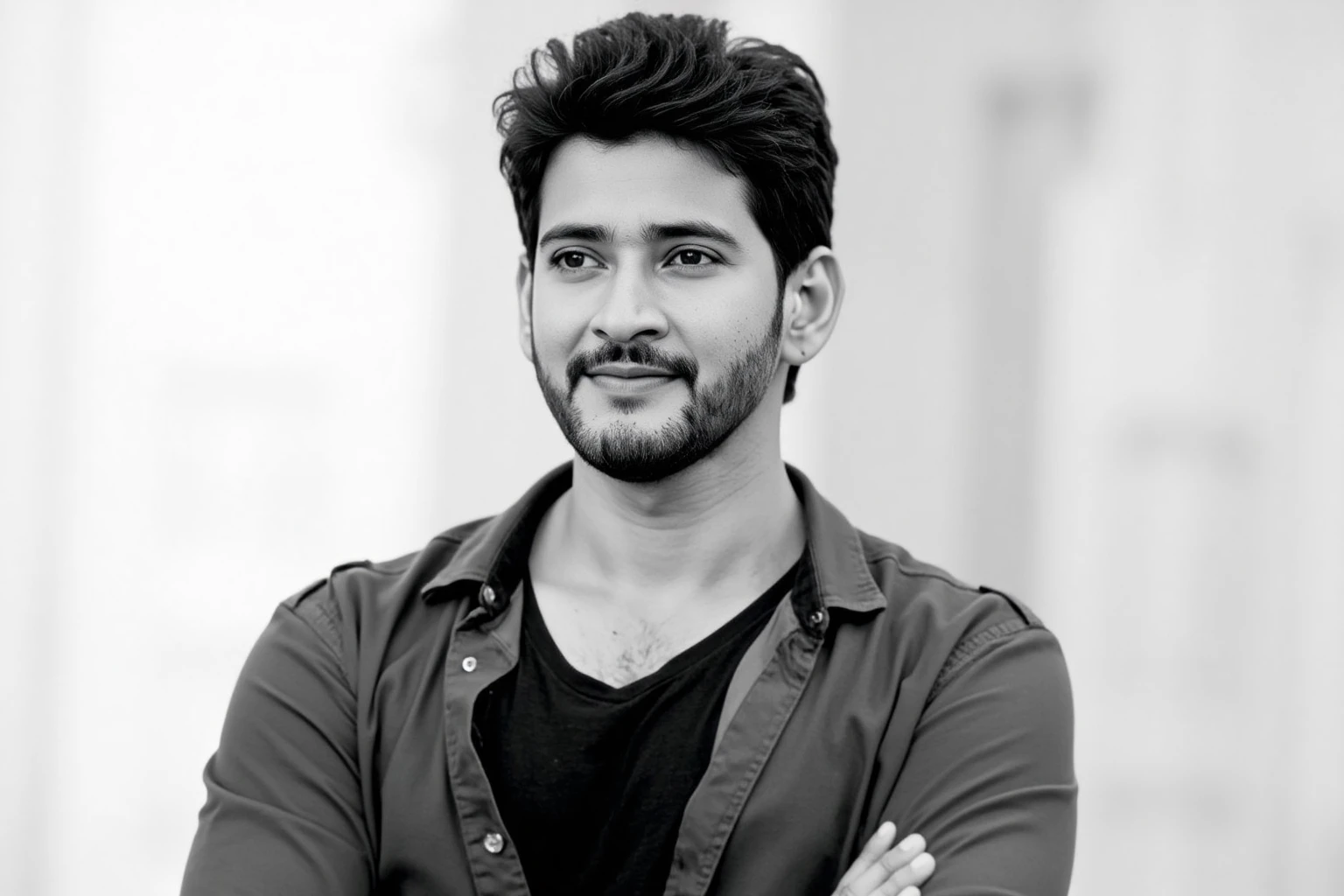 Close-up black and white portrait of ssmaheshbabuukohwx, with a naturally styled, slightly wavy dark brown hair.  He has a subtle beard and mustache, and a pleasant, slightly smiling expression, conveying a calm and approachable demeanor.  He wears a dark gray or black button-down shirt open over a darker top.  His arms are crossed across his chest, displaying a relaxed but confident posture.  The background is softly blurred, and out of focus, creating a stark contrast with the clear, detailed image of the subject.  The lighting is subtle and even, highlighting his facial features without harsh shadows.  Classic portrait style, emphasizing the subject's features with a smooth, continuous tone.  Photograph, likely taken from a slightly elevated position, showcasing shallow depth of field and using natural light.  The image's mood is serene and introspective, with a contemplative atmosphere.