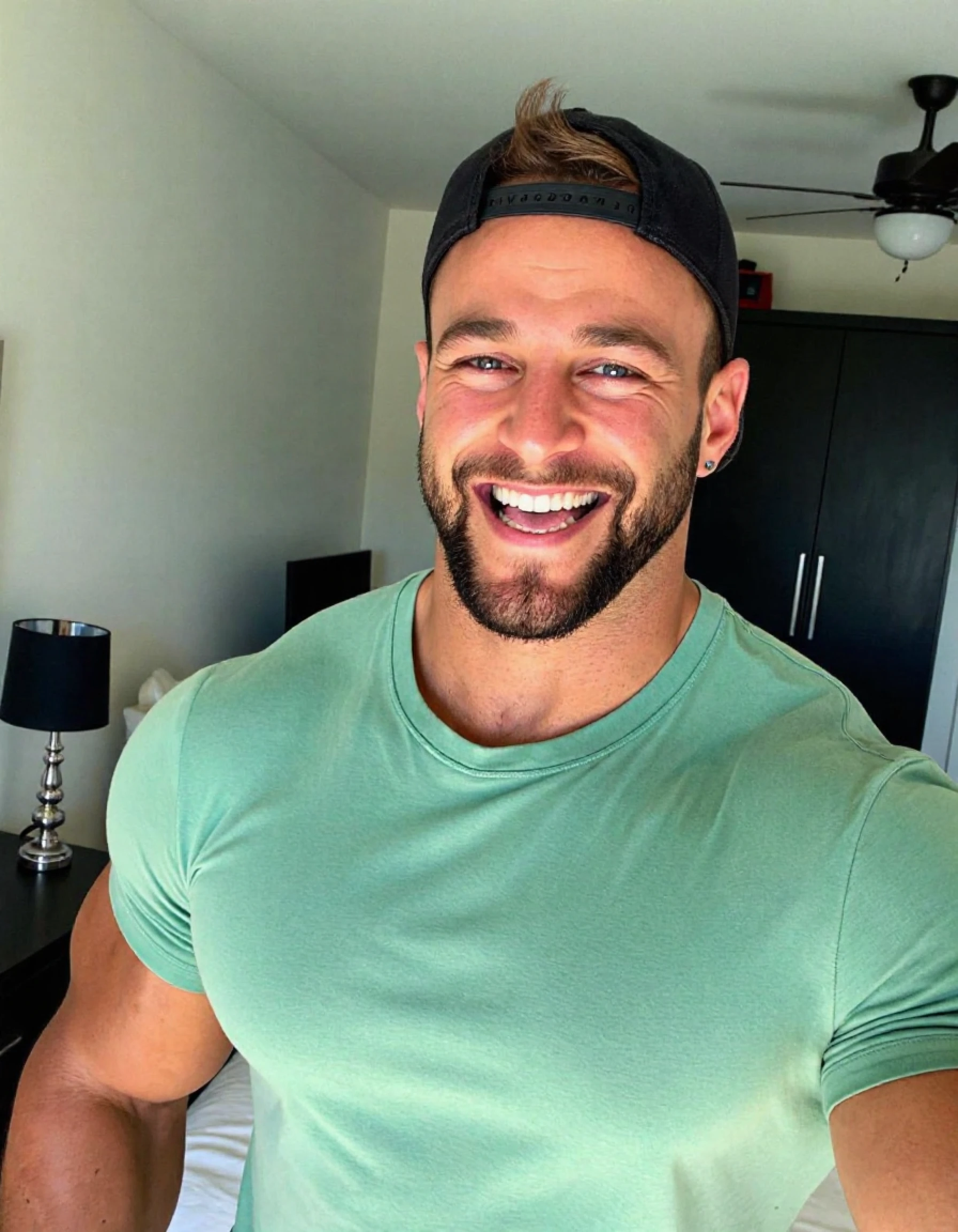 ericjanicki a man taking a selfie. he is handsome. he is muscular. he is a bodybuilder. he is wearing a green t-shirt. he is wearing a black backwards cap.  he is looking foward. he is looking straight ahead. he is smiling. he is sticking his tongue out of his mouth. he is in a bedroom. it is daytime.