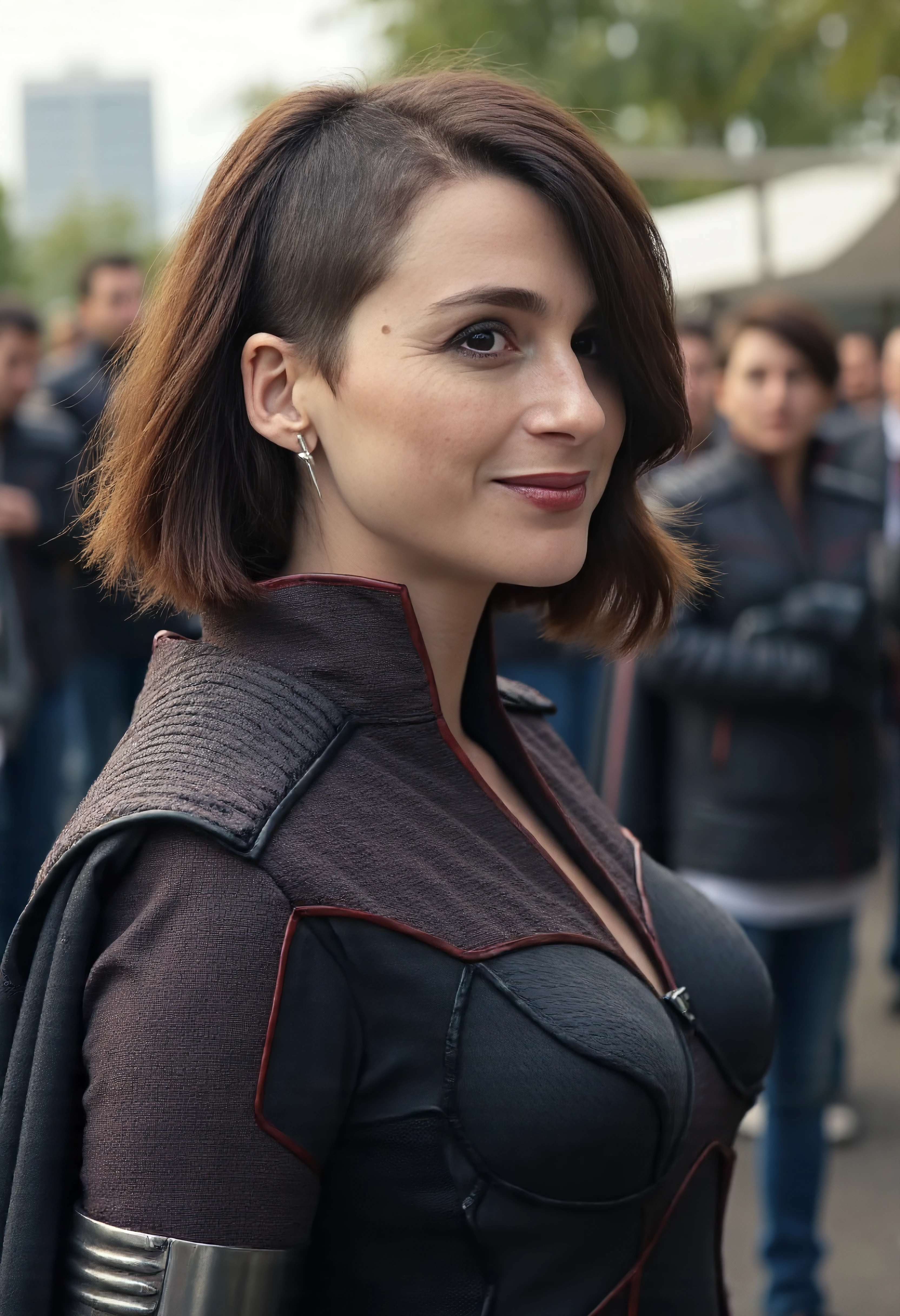 The image is a portrait of stormfront woman posing for a photo ,She has brown sidecut hair,She is wearing jumpsuit with a cape.She is outdoors with a crowd around her. She is looking at viewer. Amateur photography.She has a subtle smile. She has one arm up.