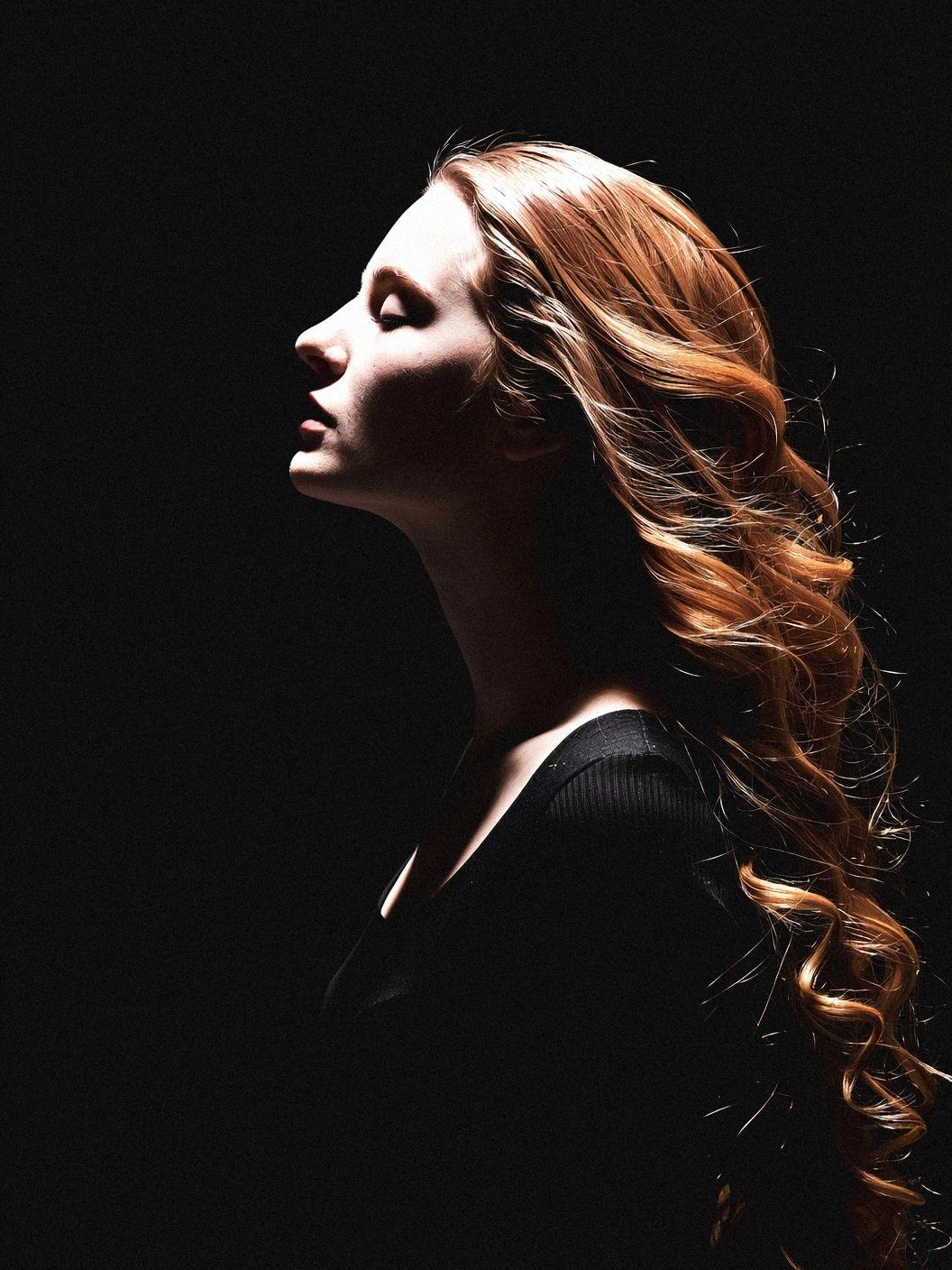 A photo-realistic portrait of a woman with long, wavy, reddish-brown hair in a monochromatic setting, taken from a profile camera angle. the image is focused on her face and upper body, with a dark background providing a stark contrast. the woman appears to be in her mid-twenties, with pale skin and long, flowing hair. her eyes are closed, and her expression is serene and contemplative. the lighting is dramatic, casting shadows across her face, highlighting her features and the texture of her hair. the overall mood is somber and melancholic, evoking a sense of loneliness and isolation.

1girl, solo, long hair, simple background, red hair, profile, black background, from side, profile picture, face, silhouette, monochrome, dark background, profile photography, shadow, portrait, portrait photography

camera_angle: profile, art_style: photo realistic, location: unknown, background: dark background with subtle shadows, text: NA, distance_to_camera: close up, clothing: dark clothing, image_composition: middle, pants: NA;NA, accessory: N/A, shoes: N//A, action: standing, facing_direction: facing away;facing away, eye_direction : NA;na, facial_expression: serene; contemplative, ear: n/A;n/a", eye_color: NA>, gender: 1woman, hair_color : red hair;brown hair, hair style: long wavy hair, race: light skin;dark skin, body: slim