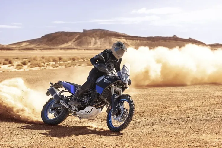 arafed motorcyclist riding a dakar motorbike in the desert, big windscreen, mud dirt tyres, skid plate, one yoshimura exhaust, no luggage, yamaha, blue and black fairing, kicking up dirt, rider using adventure gear, rider using enduro boots and helmet