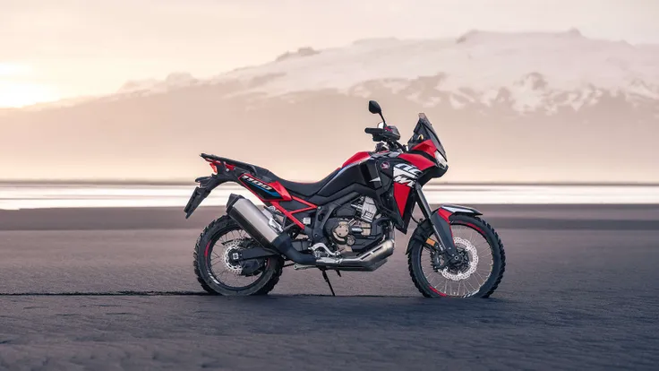 Standing alone arafed adventure motorcycle with mountains background, big windscreen, mud dirt tyres, one exhaust, honda, dakar motorbike, red fairing