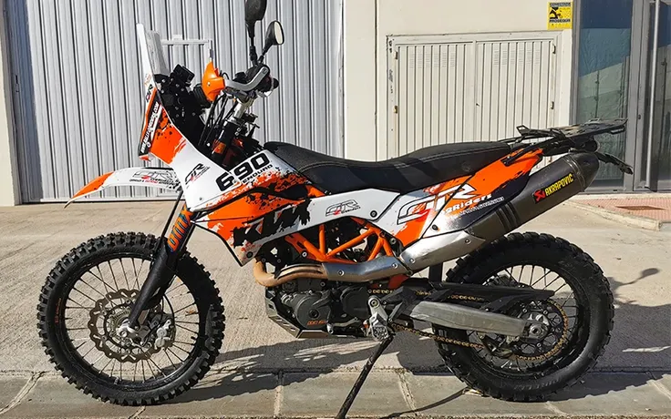 Standing alone arafed adventure motorcycle, garage background, rally dakar, big windscreen, mud dirt tyres, one yoshimura exhaust, ktm decals, stripes, orange fairing