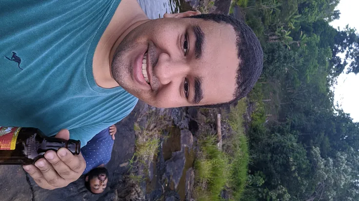 Raziel segurando uma cerveja, no meio do mato perto do rio