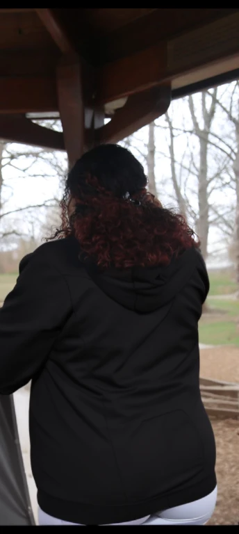 there are two people standing under a shelter talking to each other, photo still of behind view, shot from the back, view from the back, seen from the back, back of the hair, from the back, wearing a black hoodie, with curly red hair, facing away from came...