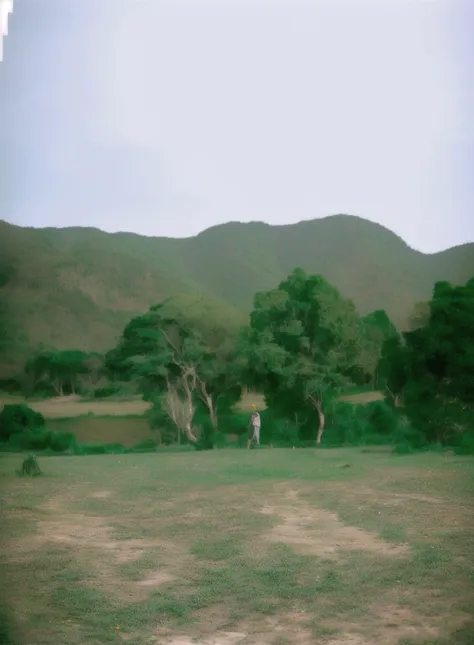 there is a man that is standing in the grass with a frisbee, hills in the background, landscape in background, hill with trees, jungle in background, trees in background, jungles in the background, landscape 35mm veduta photo, moutain in background, landsc...