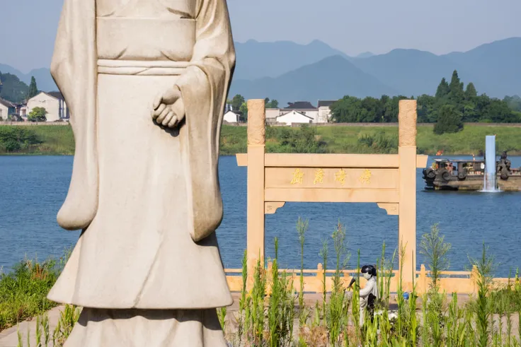 statue of a man in a robe standing by the water, torii in the background, guardian of the holy lake, large stone statue of heroe...