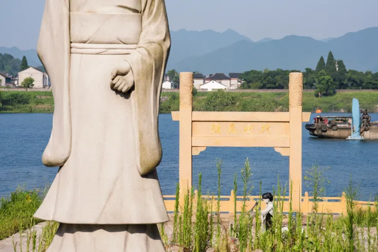 statue of a man in a robe standing by the water, torii in the background, guardian of the holy lake, large stone statue of heroe...