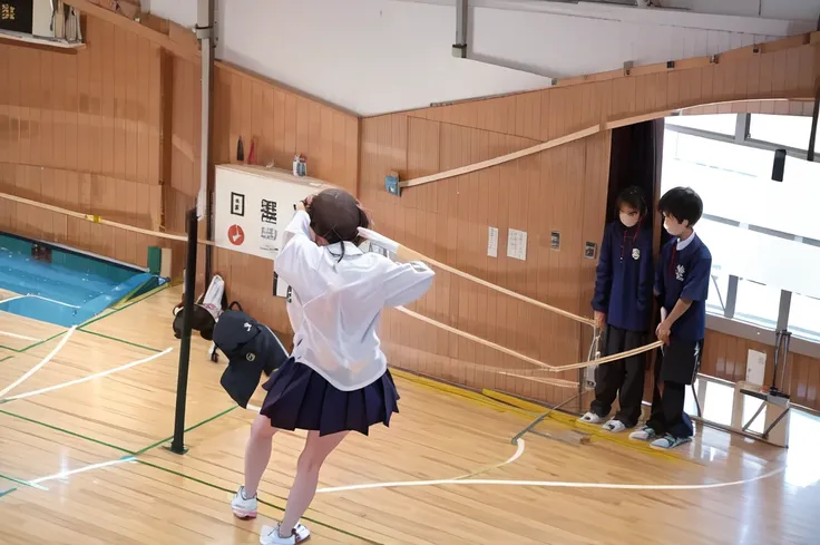 A female student in a sailor uniform is watching a physical education class in the gymnasium because she is feeling unwell