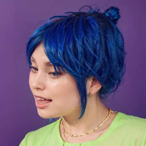 The image features a vibrant portrait of a young woman with striking blue hair styled in a dynamic, tousled look. Her makeup is bold and colorful, with yellow and blue eyeshadow that complements her hair, and a natural pink lip color that adds a soft touch...