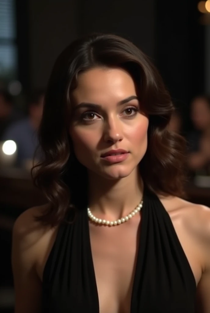 A close-up of a woman with dark brown, wavy hair wearing a black halter-neck dress. She has a serious and focused expression, her lips slightly parted. The woman is adorned with a delicate pearl necklace. The background is slightly blurred, with dark tones...