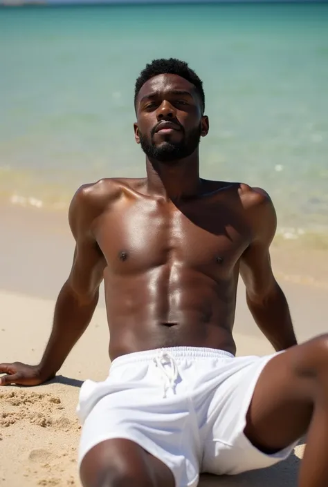 A black man posing shirtless in white shorts on the beach lying on the sand sunbathing 