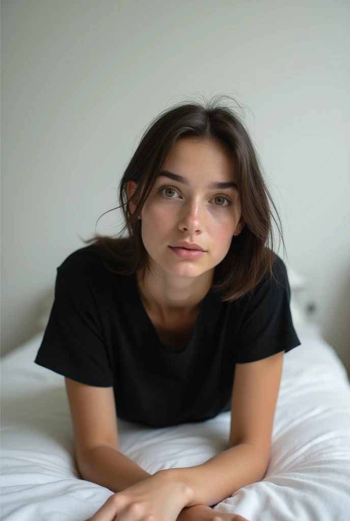 brunette, smile, flat chest, skinny face, white wall, no decoration, jean shorts, black t-shirt, lying on stomach on bed, looking at camera, photo from behind
