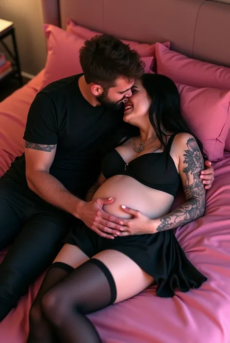 Happy pregnant goth girl wearing black crop top and mini skirt and tights and high heels while lying on a pink bed and her footballer boyfriend kissing her belly 