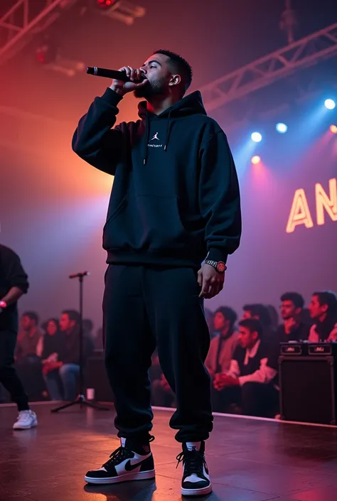 Rapper performing on stage, mic on hand, ANTF written in display board, black hoodie, joggers and jordan shoes, audience on down floor, dj at side, 