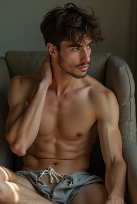 Naked young man (full body close up) sitting on a chair, one hand on the back of his neck and the other on his exposed intimate part 