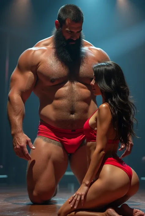 A huge hairy bearded strong muscular Brazilian mixed race man in red bulge underwear having his thighs examined by a beautiful woman in red panties crouching in front of him, in performance on a stage of a television program presented by a famous presenter...