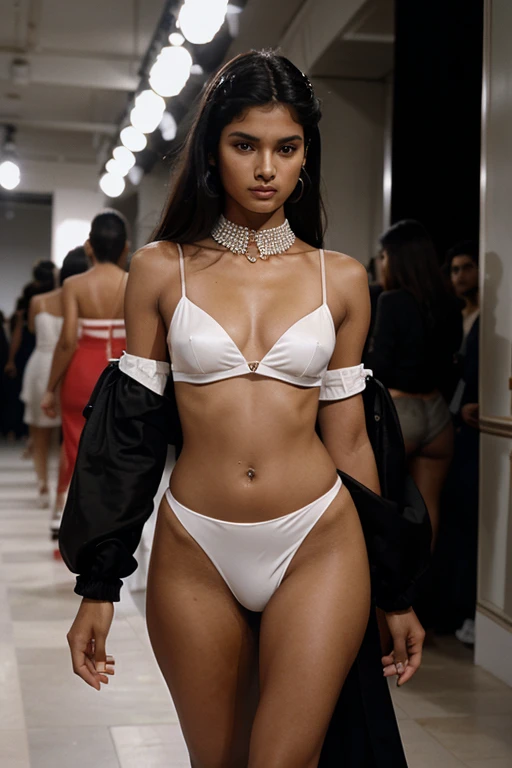 Black-and-white press photo from an exclusive 1990s catwalk show, Milan Fashion Week. Extravagant designer clothes. In the foreground is a beautiful half-Indian female model, 20 years old.