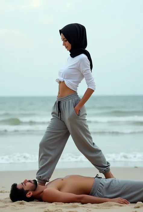 Black headscarf on the beach, grey baggy sweatpants, white long sleeve t shirt, barefoot, sexy and skinny woman. Man lying on his stomach in front of woman. Woman puts her foot on the front of man&#39;s sweatpants. 