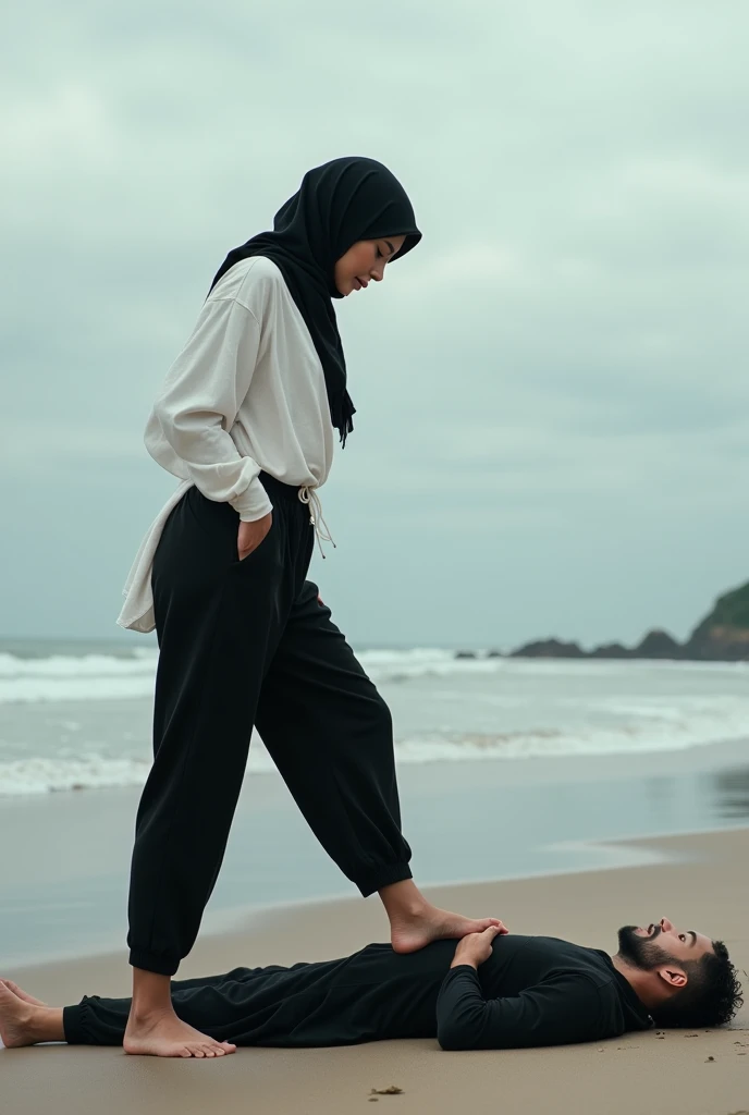 Black headscarf on the beach, black baggy sweatpants, white long sleeve t shirt, barefoot, sexy and skinny woman. Man lying on his stomach in front of woman. Woman puts her foot on the front of man&#39;s sweatpants. 