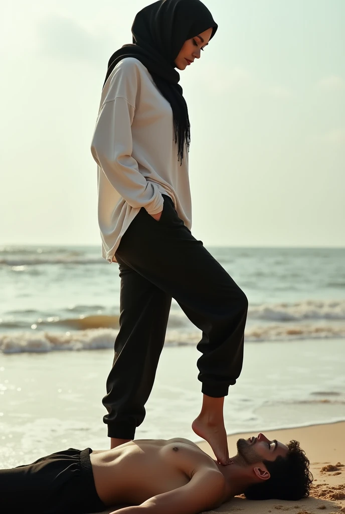 Black headscarf on the beach, black baggy sweatpants, white long sleeve t shirt, barefoot, sexy and skinny woman. Man lying on his stomach in front of woman. Woman puts her foot on the front of man&#39;s pants. 