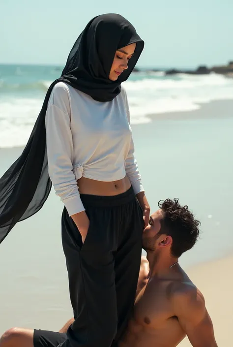 Black headscarf on the beach, black baggy sweatpants, white long sleeve t shirt, barefoot, sexy and skinny woman. Man lying on his stomach in front of woman. Man kisses woman&#39;s feet. 