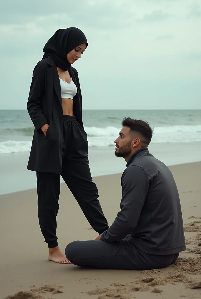 Black headscarf on the beach, coat pants head, barefoot sexy skinny woman. Man sitting in front of woman. Woman puts her foot on the front of man&#39;s sweatpants. 