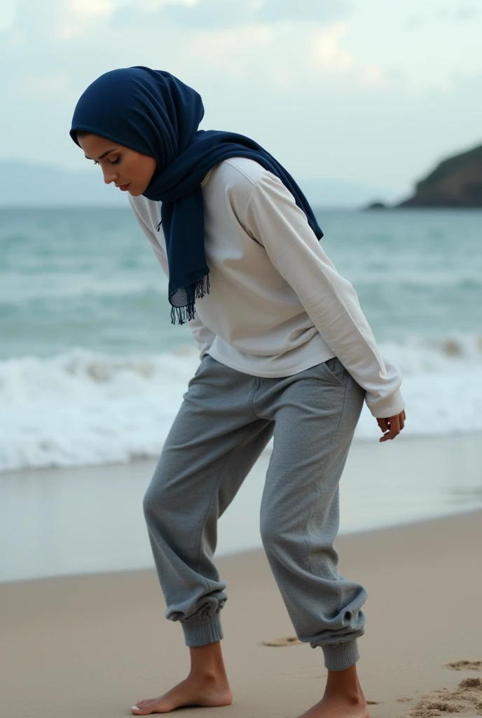 Navy blue headscarf on the beach, grey baggy sweatpants, white long sleeve t shirt, barefoot, Sexy skinny woman bent over. 