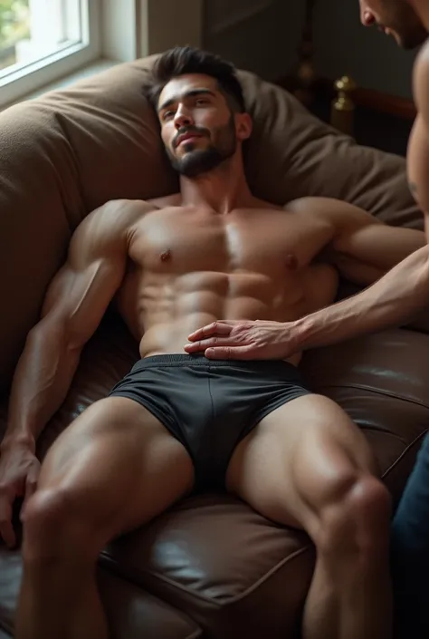 A jock in boxers sits on a sofa and a man touches his bulge in his boxers 